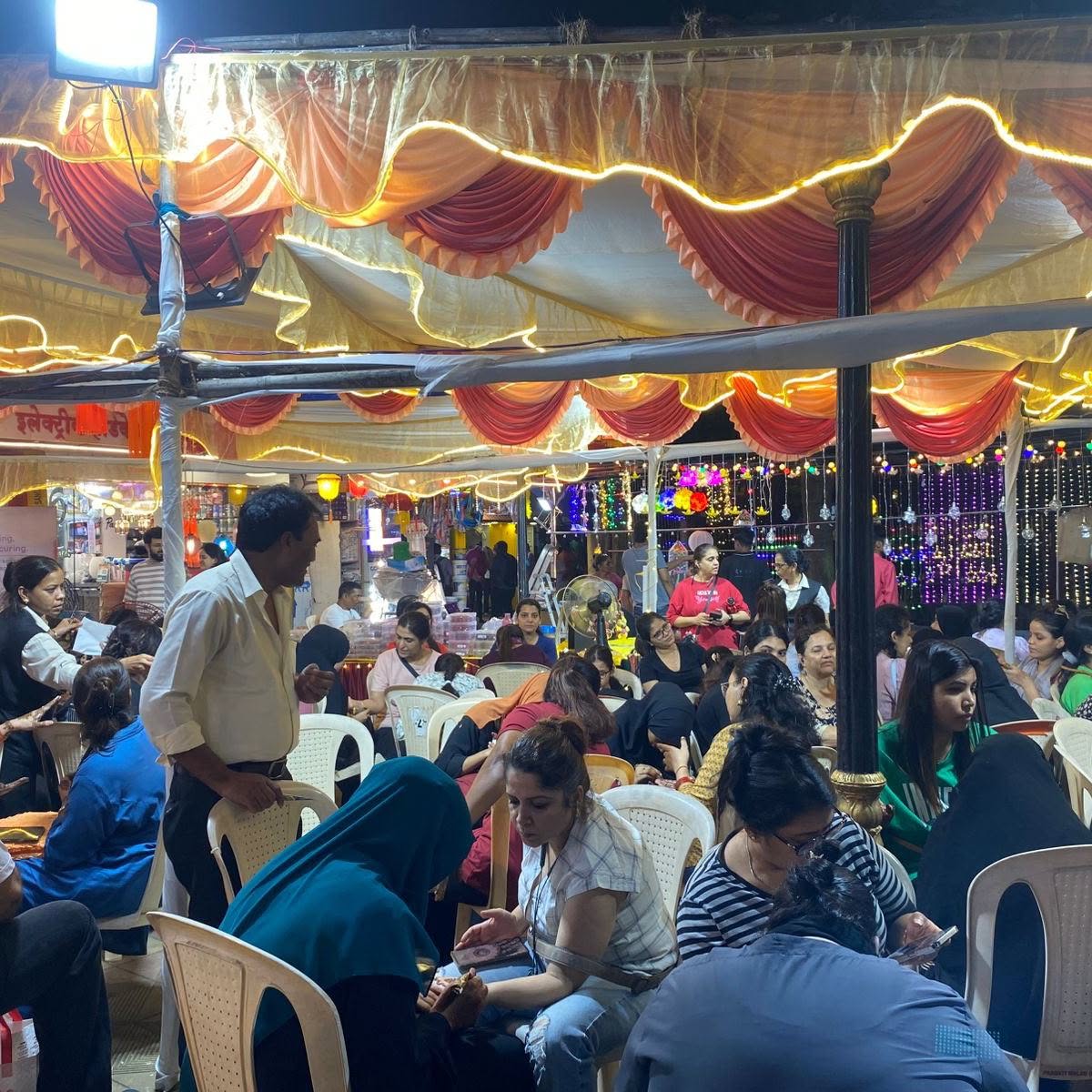 Women getting mehendi done under a lit canopy at the Mehandi Mela 2025